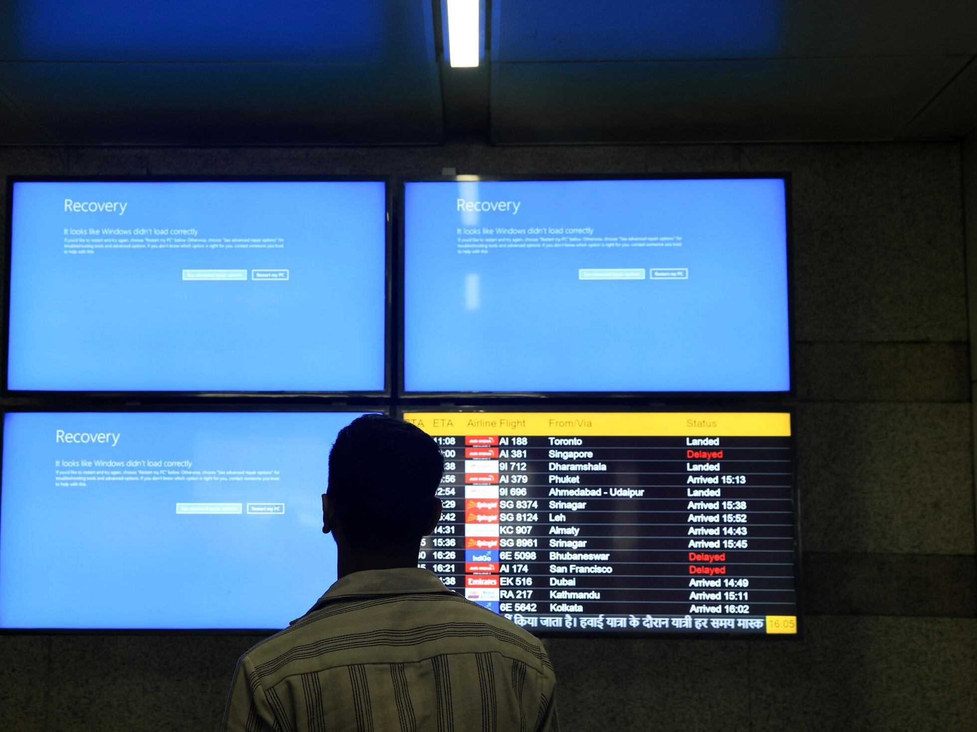 Passenger at airport looking at multiple crashed flight status screens after a system error.