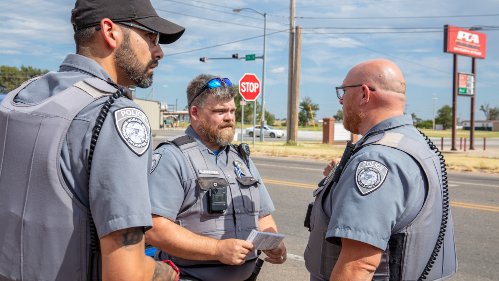 Two law enforcement officers talking roadside, both wearing body cameras visible on their uniforms, illustrating field deployment.