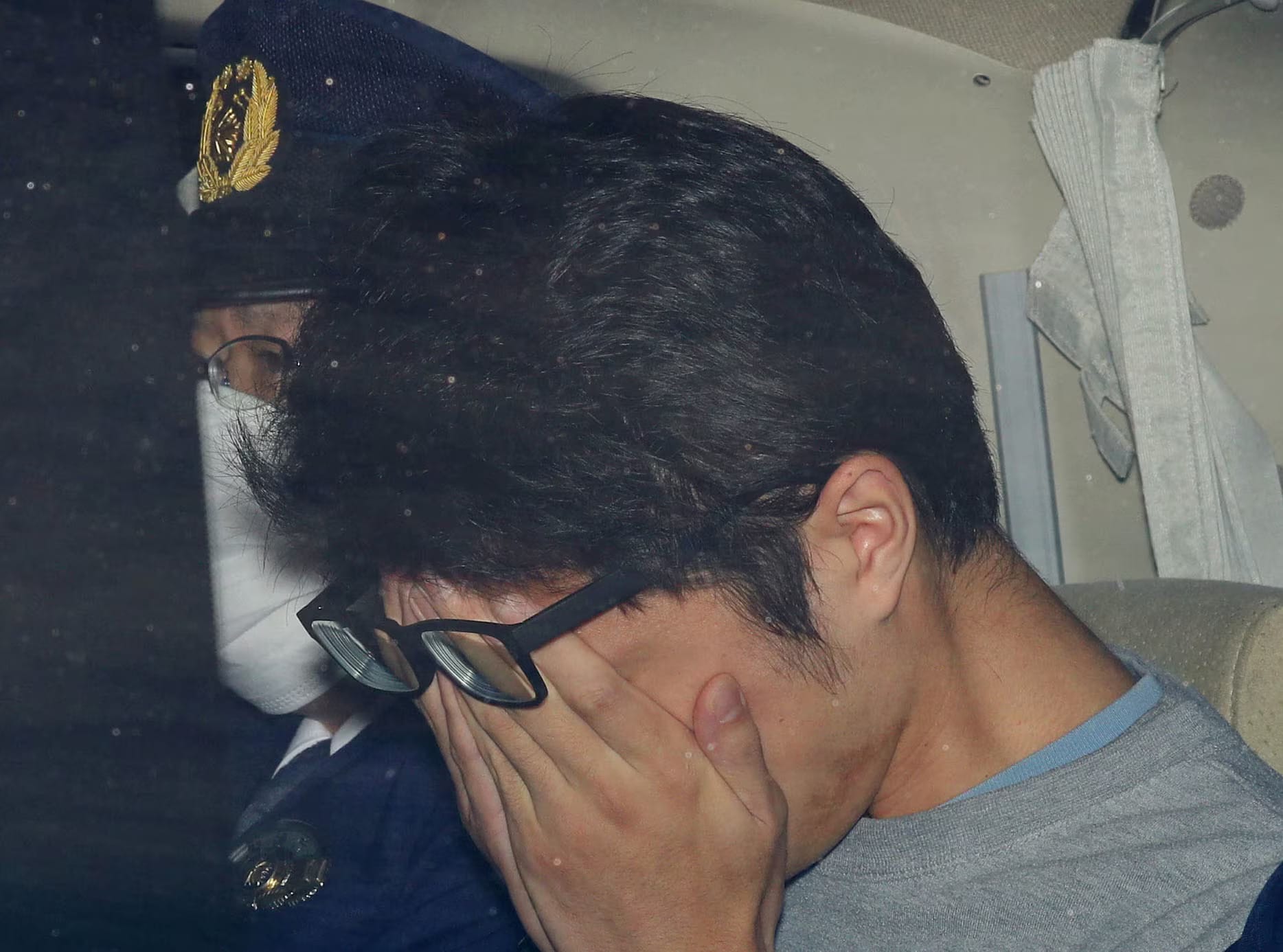 Side view of Shiraishi covering his face in a police car.