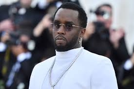 : Sean Combs wearing a white suit and sunglasses at a red-carpet event, maintaining public appearances amid controversy.