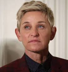 Ellen DeGeneres looking serious, wearing a dark blazer and shirt.