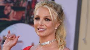 Britney Spears smiling at a red carpet event, wearing a red dress and silver choker.