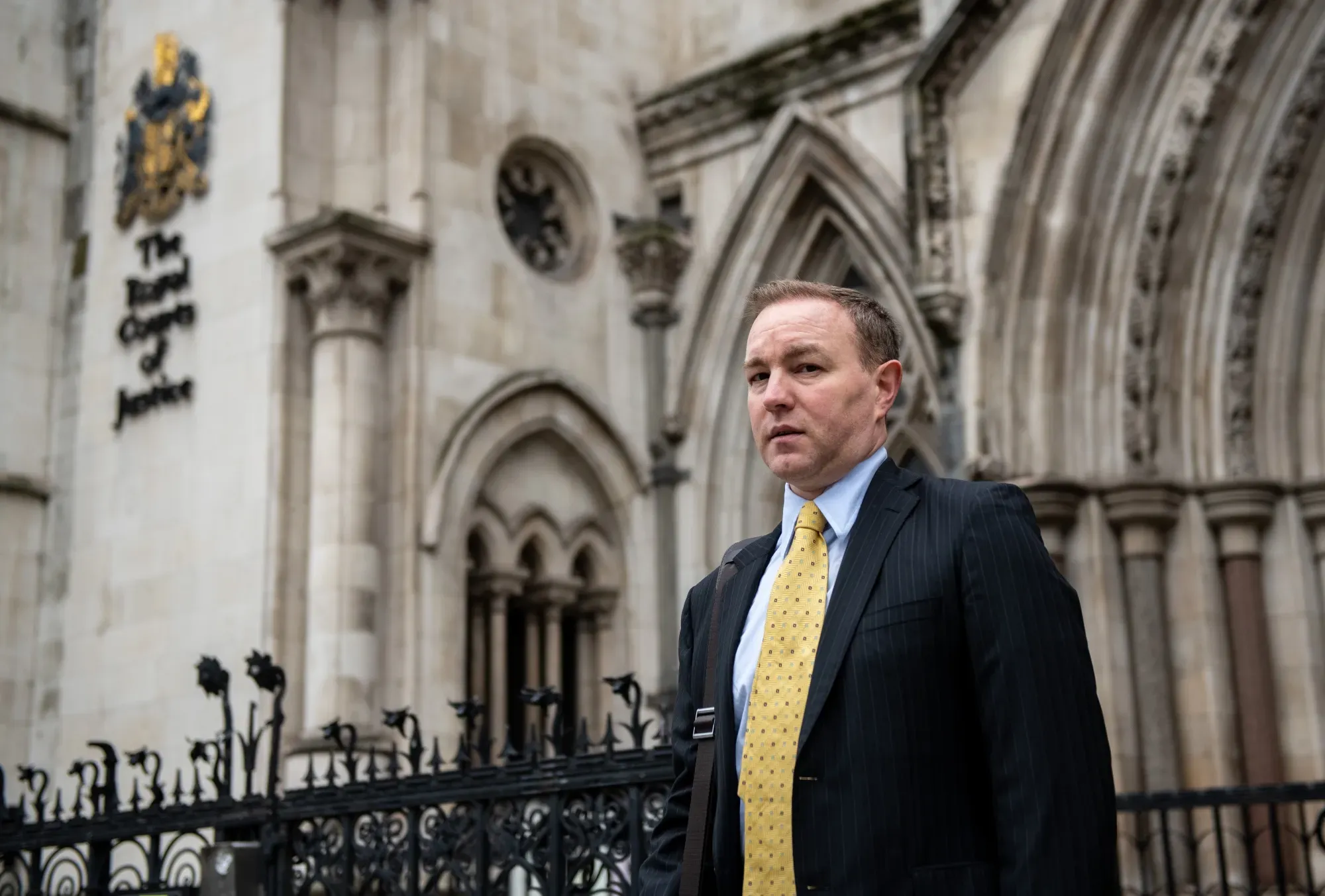 Man in dark suit and yellow tie walking in front of ornate courthouse architecture.