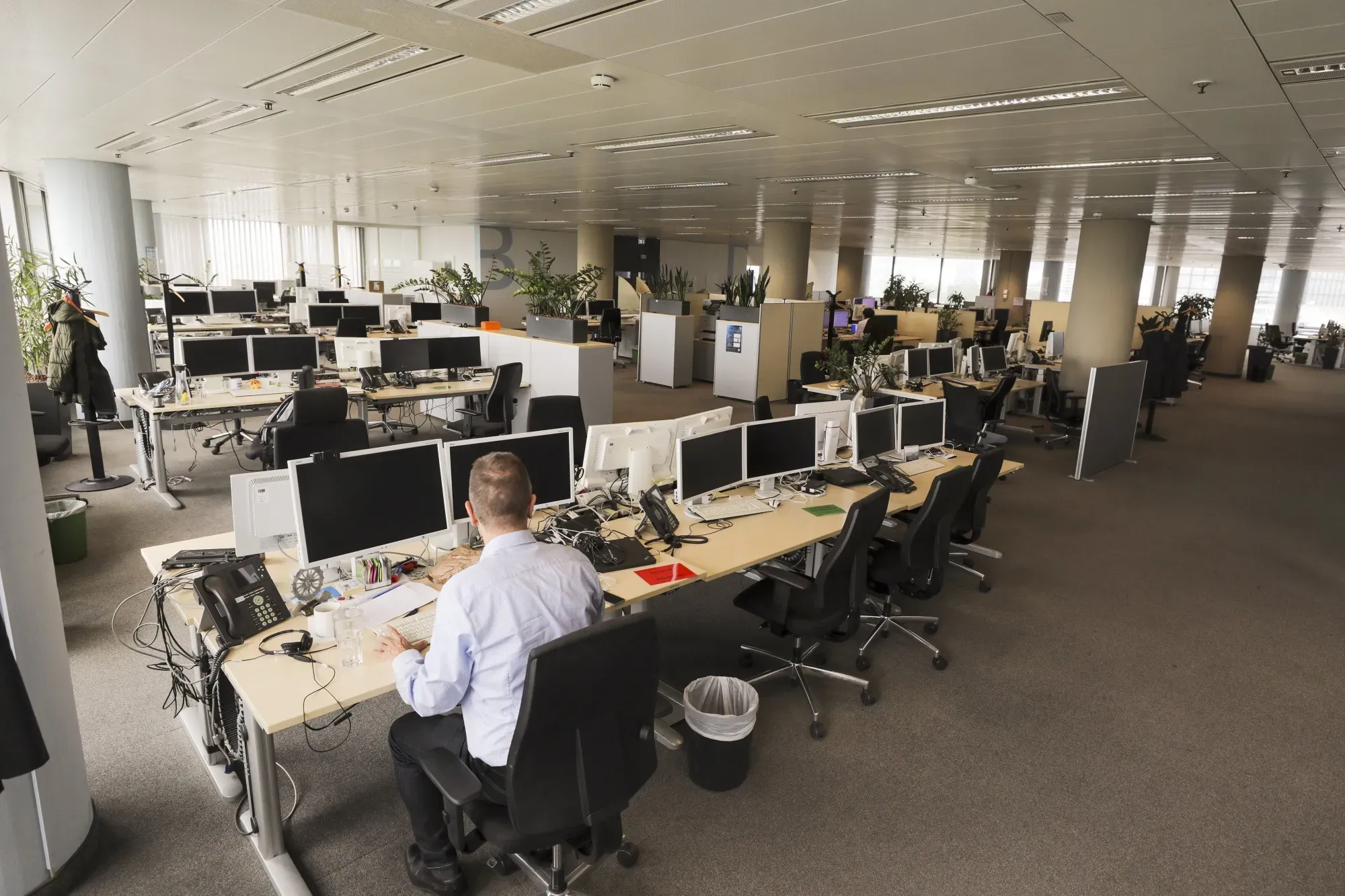 A nearly empty modern office space with rows of vacant desks and computers, as a lone worker sits facing multiple monitors.