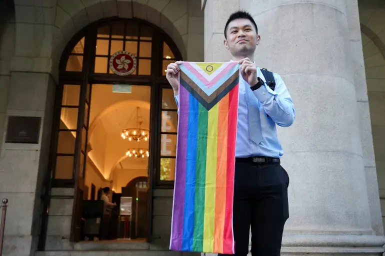 Man stands proudly holding a Progress Pride flag outside court