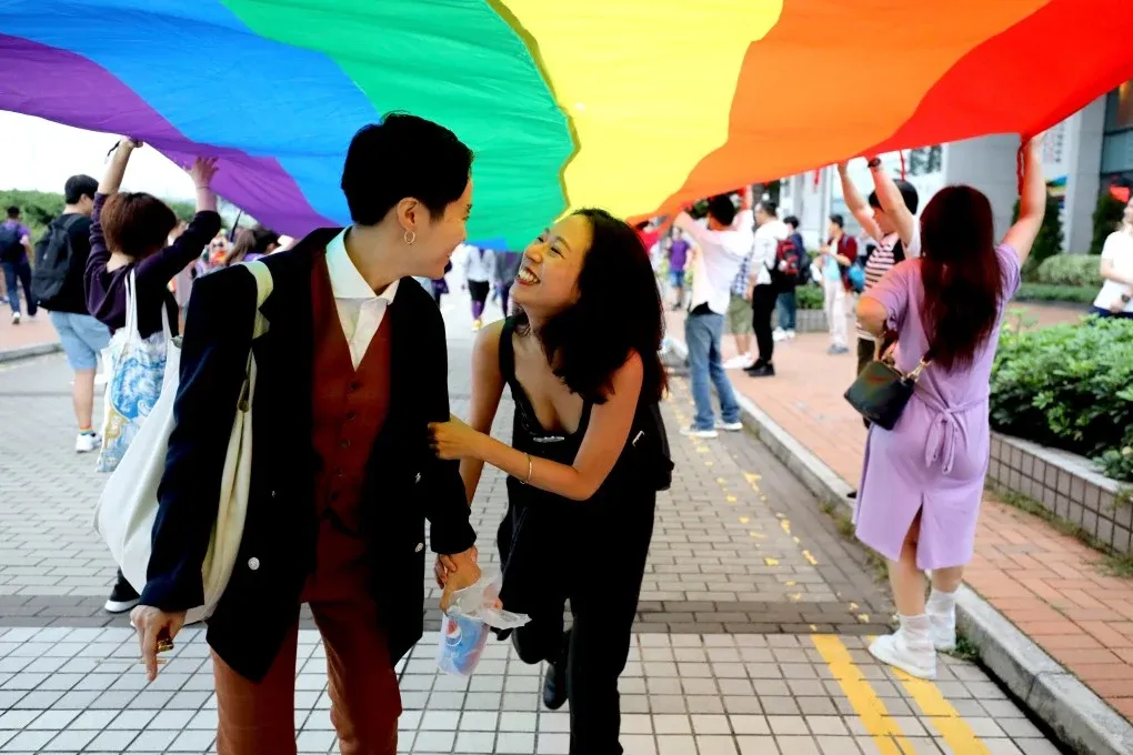 Two women smile and laugh under a giant pride flag