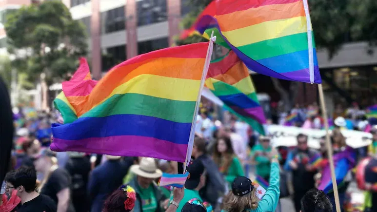 People waving rainbow flags at a crowded pride rally