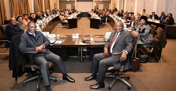 President Cyril Ramaphosa and senior cabinet ministers sit in a large U-shaped conference room filled with officials.