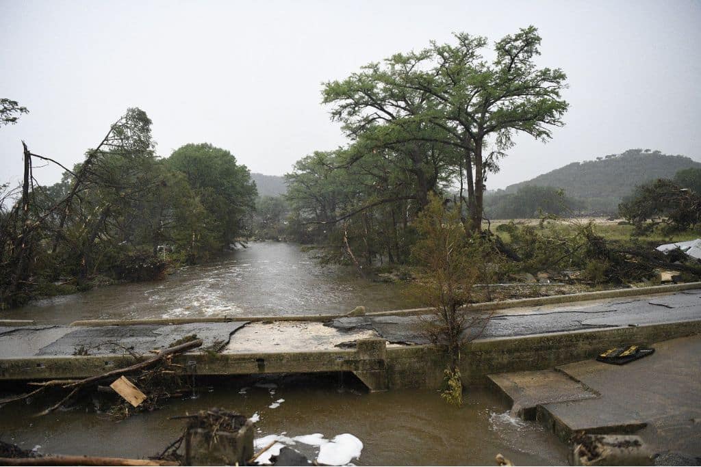 Broken road infrastructure surrounded by rising floodwaters and fallen trees.