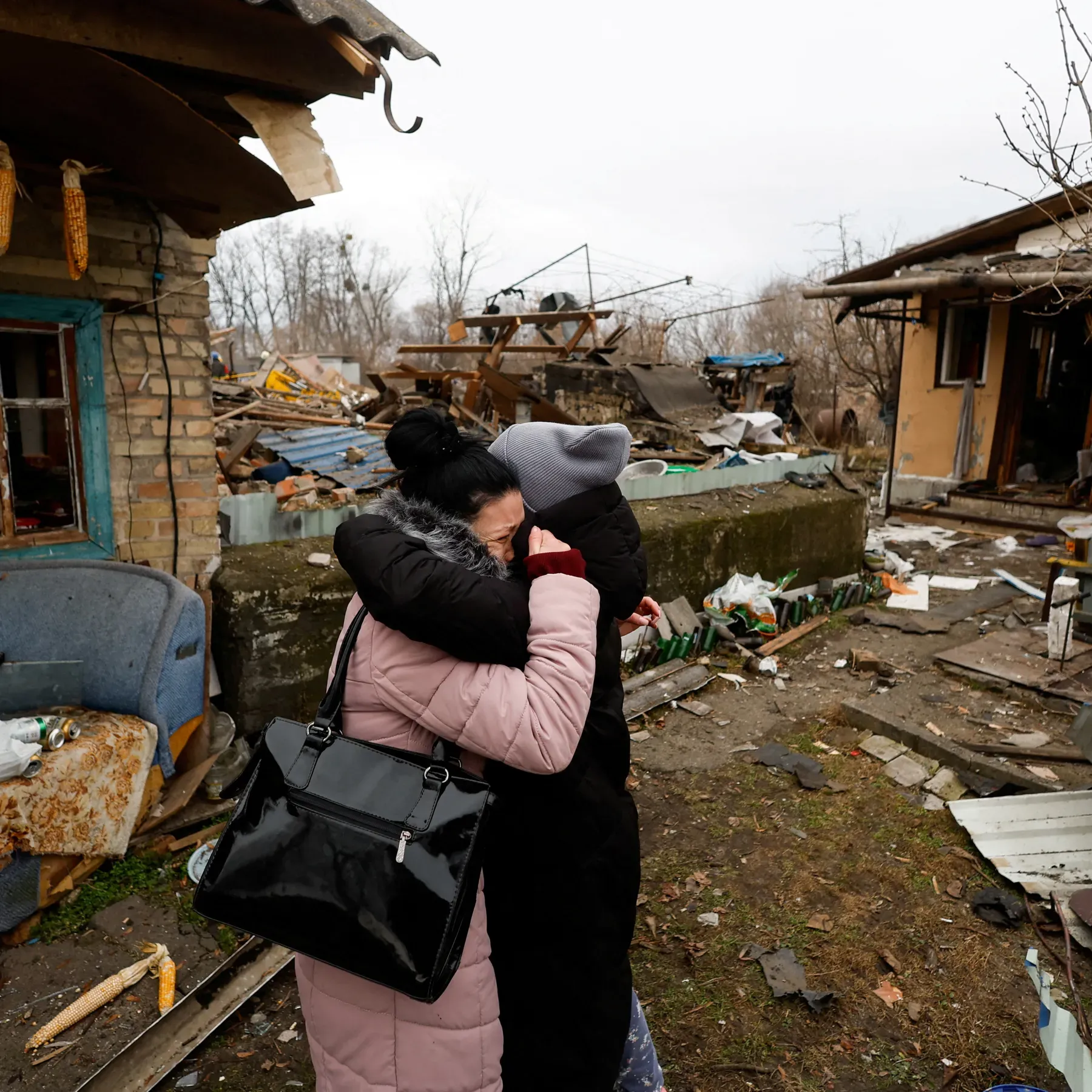 Civilians hugging and comforting each other amid rubble from a drone strike, with emergency responders in the background.