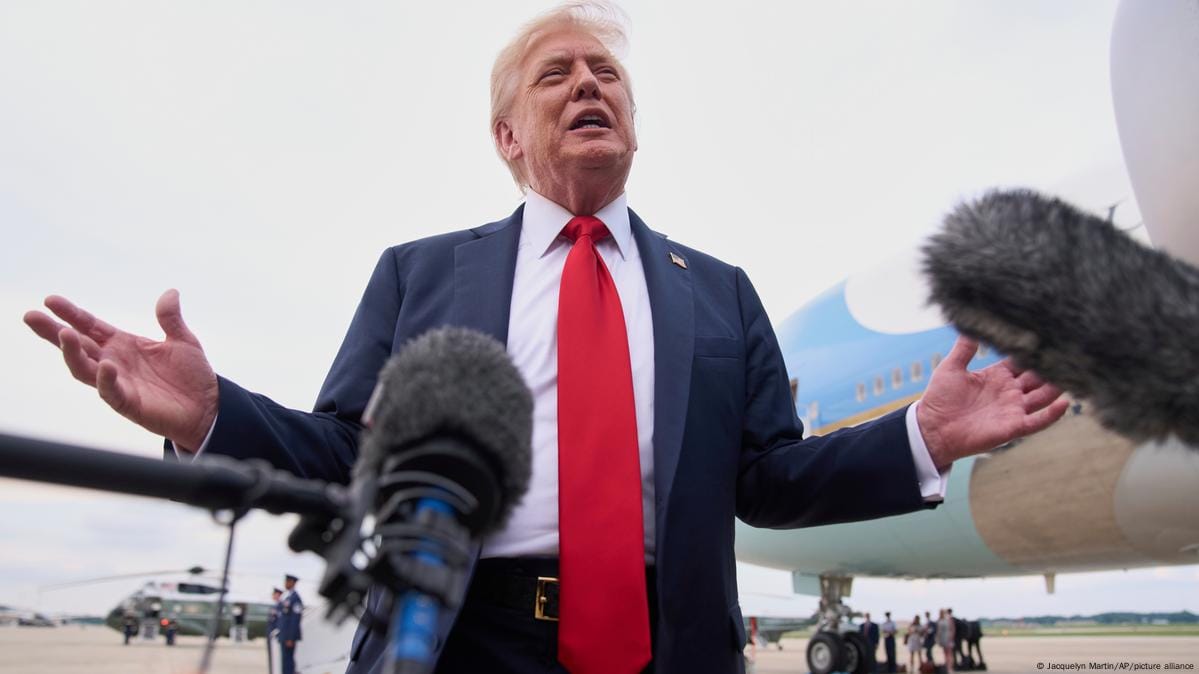 Donald Trump stands in front of Air Force One, speaking to reporters with microphones surrounding him.