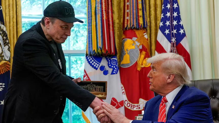 Elon Musk hands Donald Trump a commemorative plaque while Trump gestures intently, surrounded by military banners in the White House’s Oval Office.