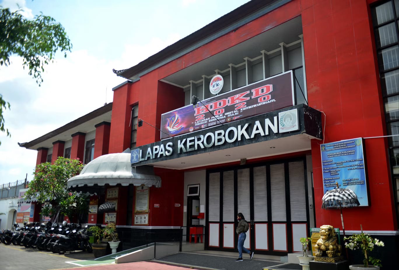 Front view of the red Kerobokan Prison building in Bali with signage and motorcycles parked.