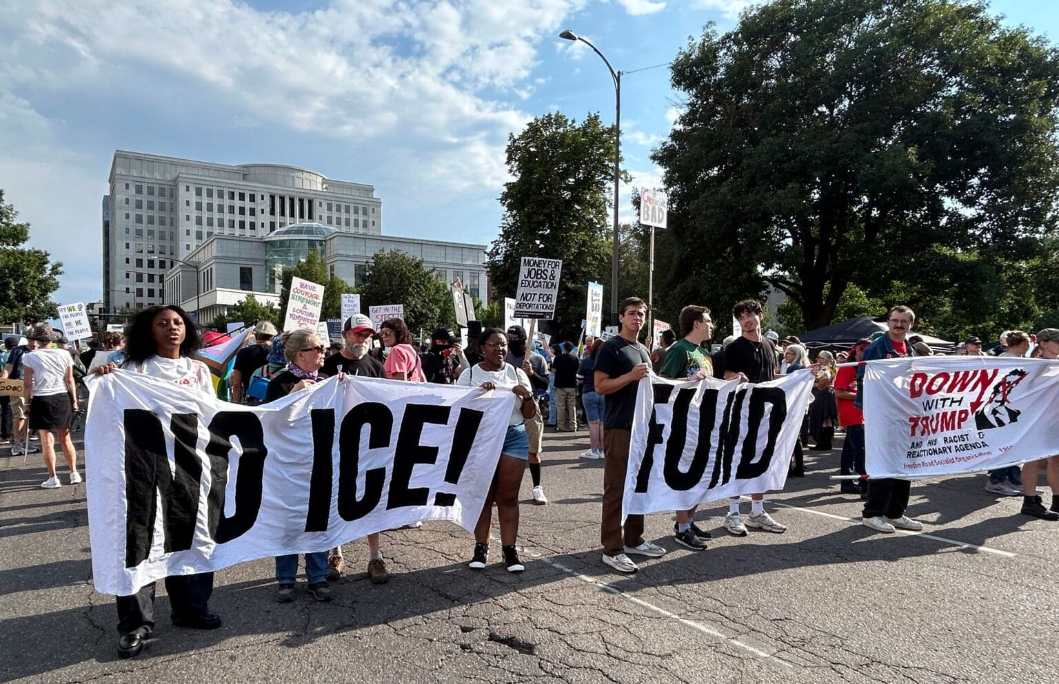 Marchers in Denver holding large banners reading “FUNO!” or “NO ICE!” in a public square near the state capitol.