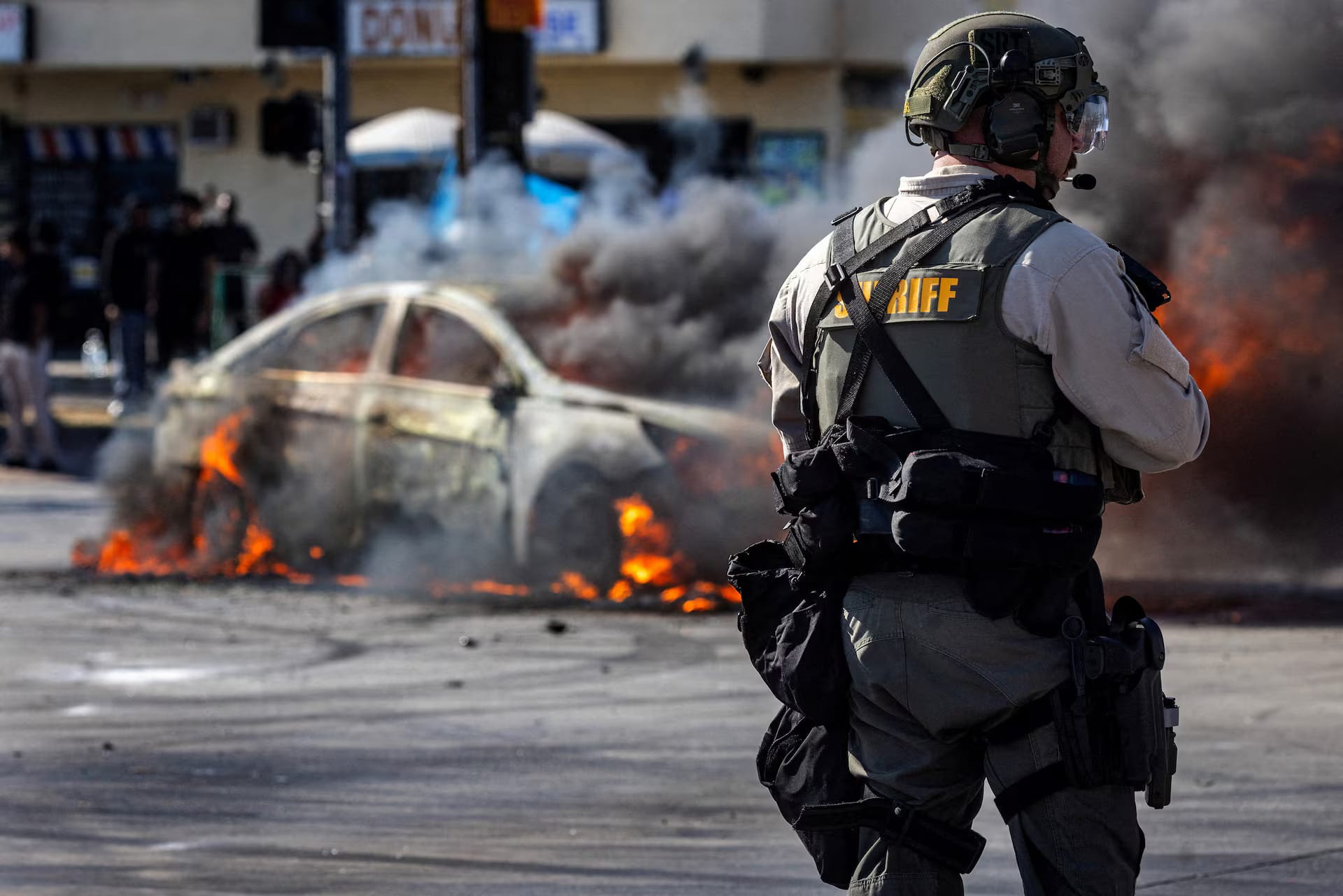 A vehicle ablaze while riot police and protesters clash during LA-area demonstrations.