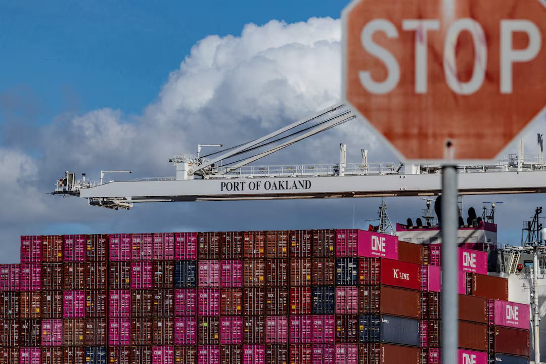 Cargo containers on a dock under a “stop” sign, illustrating trade logistics amid policy uncertainty.