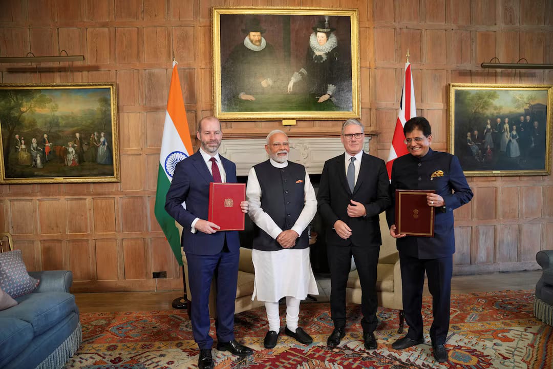 Indian and British officials holding FTA documents in a formal signing setup.