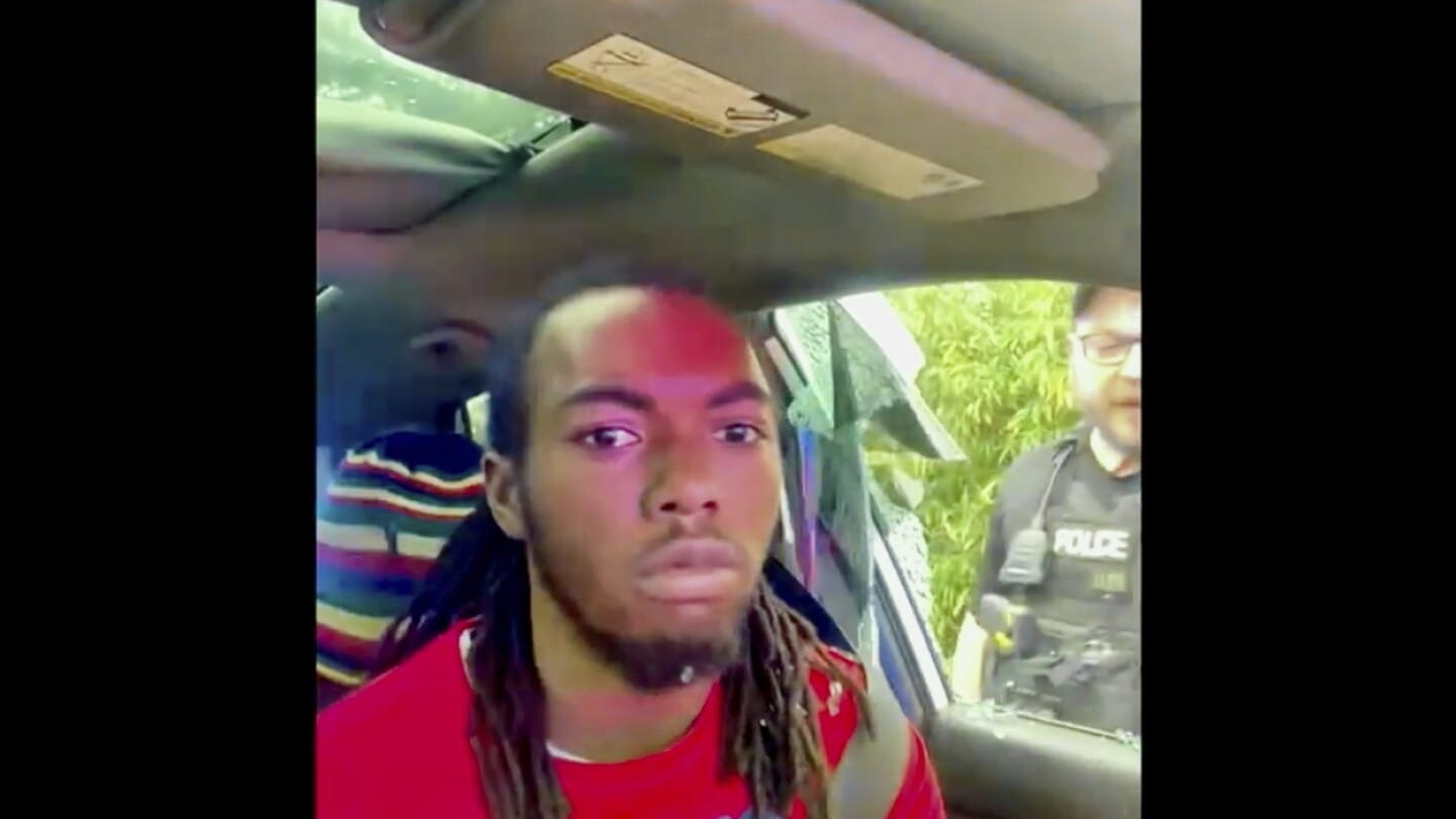 William McNeil Jr., seated in his car with a neutral expression, as a police officer stands outside his window during the controversial arrest.