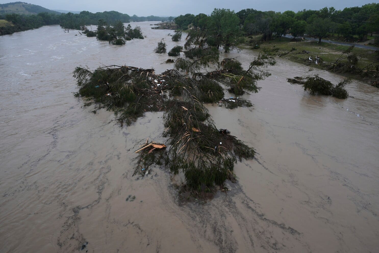 View of flood-swollen river carrying uprooted trees and storm debris downstream.