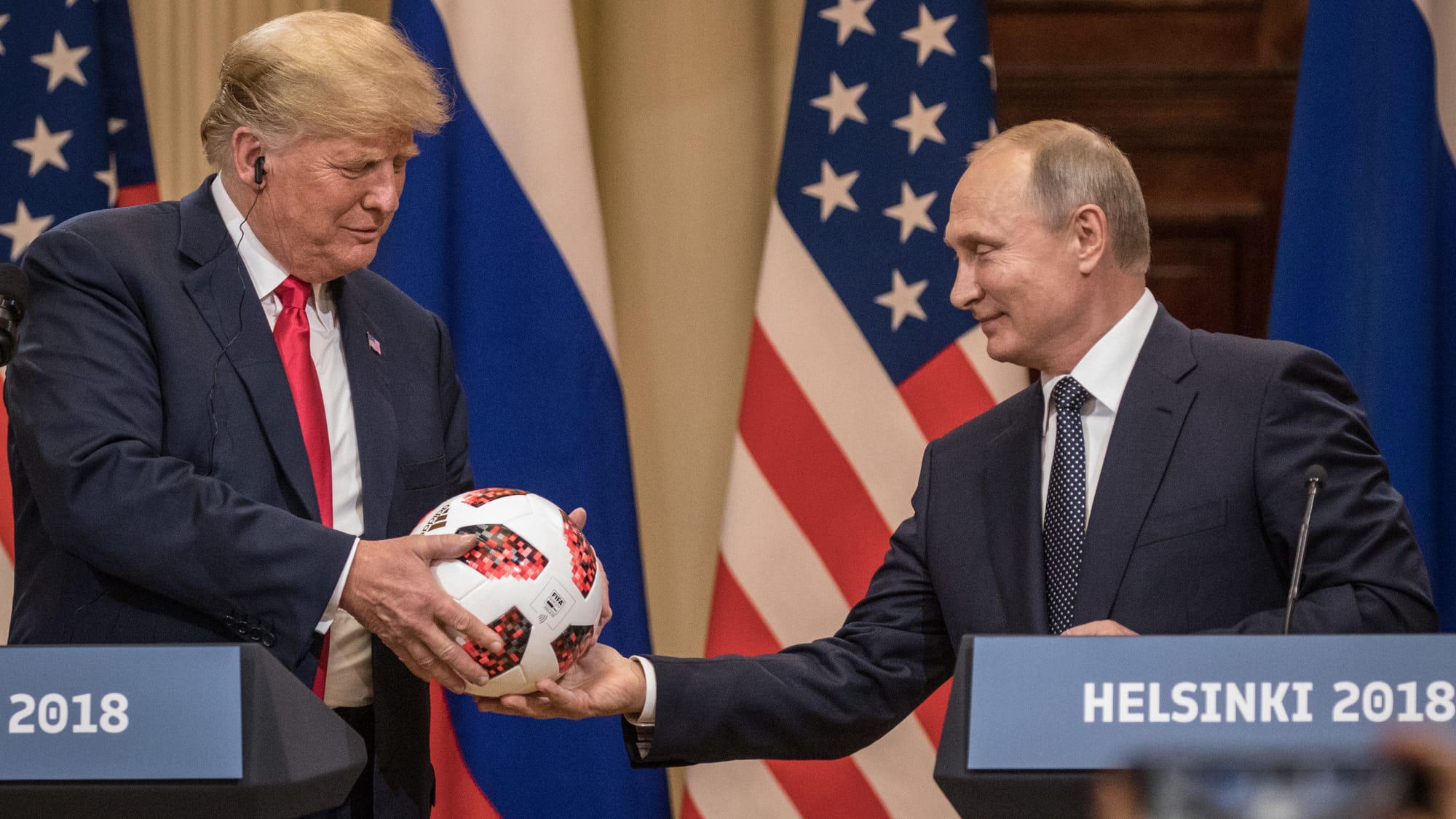 Trump receiving soccer ball from Putin with flags and microphones in background.
