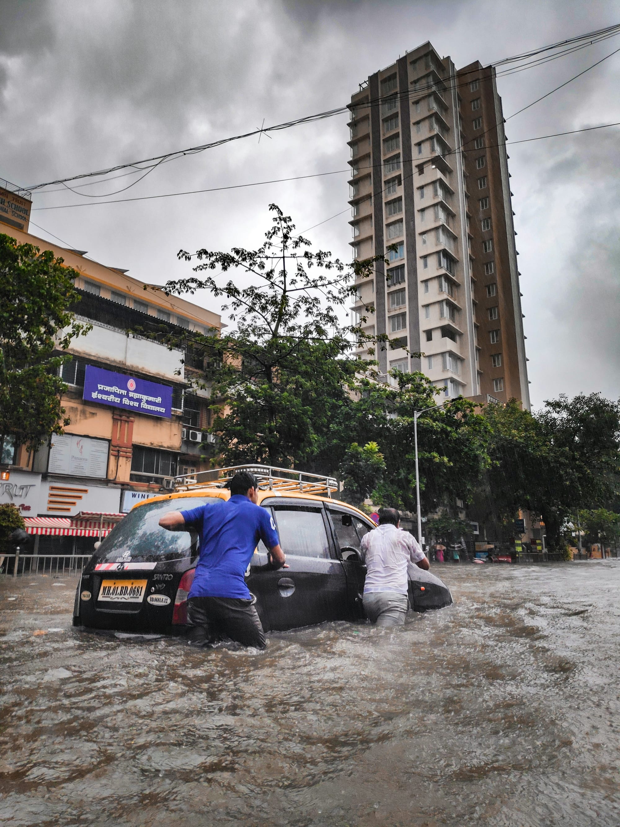 Cars partially submerged and people wading through water in a flooded Mumbai street.