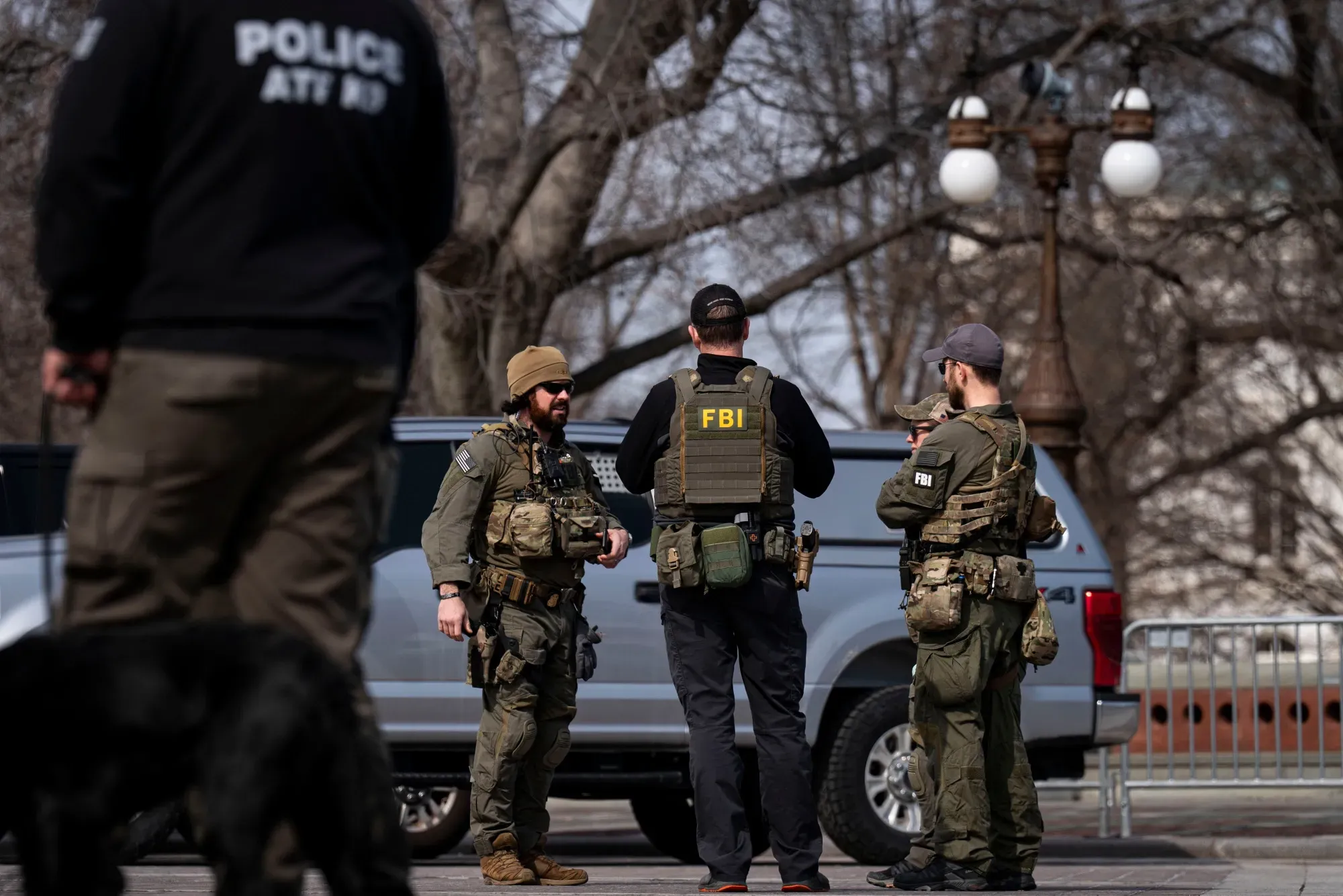 Law enforcement officers in tactical gear stand near police vehicles on a city street at night.