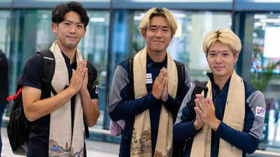 Three men dressed in coordinated sports team uniforms stand indoors, wearing beige scarves with traditional patterns.