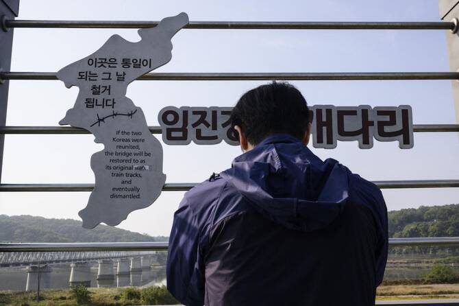 A person stands facing a fence with a cut-out map of the Korean Peninsula and Korean text.