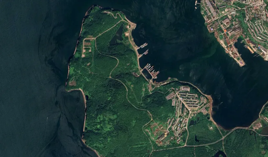 High-resolution satellite image showing Russia’s Petropavlovsk-Kamchatsky naval base on the eastern coast, including green forested areas, dockyards, submarines, and port facilities.
