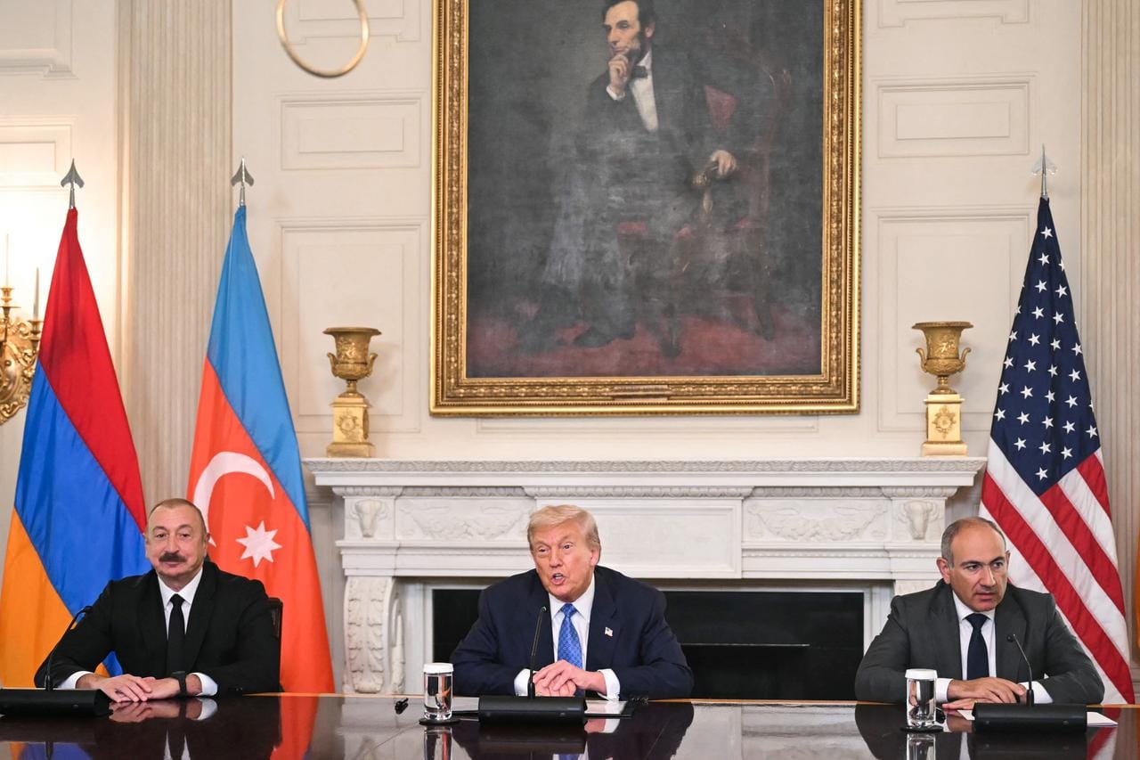 Armenian Prime Minister Nikol Pashinyan, U.S. President Donald Trump, and Azerbaijani President Ilham Aliyev sit at a long table with national flags behind them.