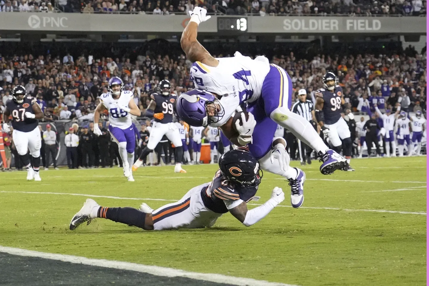 Minnesota Vikings player dives into the end zone while being tackled by a Chicago Bears defender during an intense NFL game at Soldier Field.