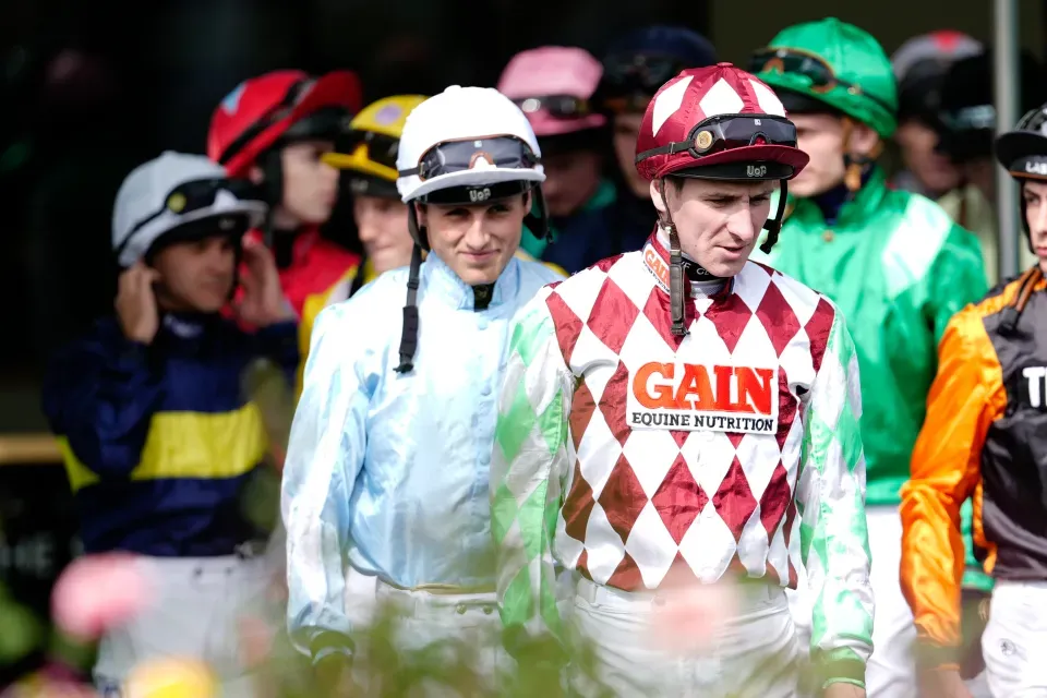 A broadcast-style shot of jockeys standing idle.