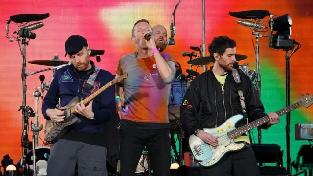 Coldplay performing live with Chris Martin singing and band members playing guitar and bass on stage.