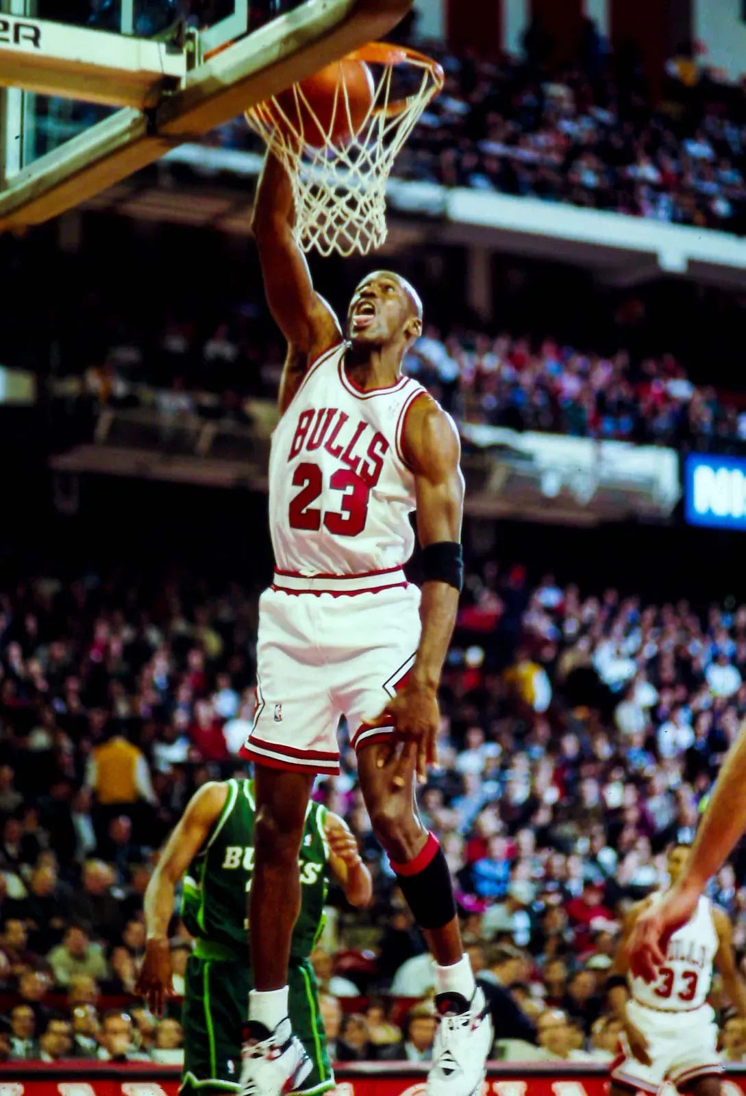 Michael Jordan, wearing his Chicago Bulls #23 jersey, leaps towards the basket for a slam dunk during an NBA game.