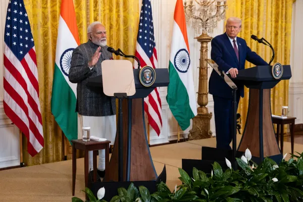 Prime Minister Modi and former President Trump stand at podiums during a joint press event, flanked by U.S. and Indian flags.
