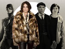 Ezra Miller shown wearing a fur coat, surrounded by their characters including The Flash, symbolizing duality between stardom and scandal.