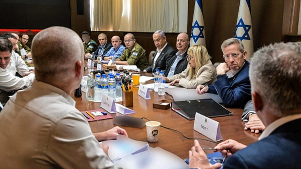 Israeli officials and military leaders gathered around a long table during a high-level security meeting, with national flags in the background.
