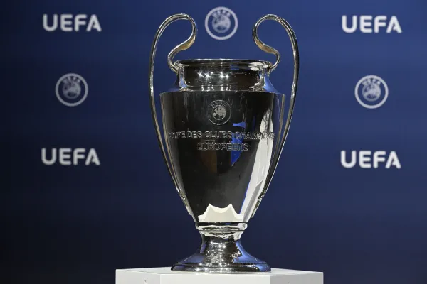 The UEFA Champions League trophy, also known as the European Cup, displayed in front of a blue backdrop with UEFA logos.