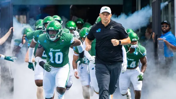 Tulane Green Wave football team, led by their head coach and captain number 10, runs out of the tunnel through smoke before a game.