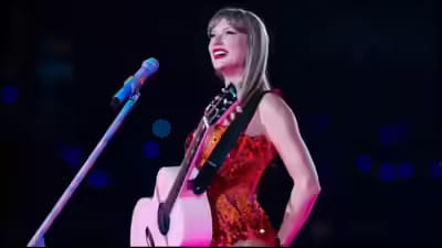 Taylor Swift performs on stage in a shimmering red dress with a white guitar, smiling brightly while captivating the crowd during her live concert.