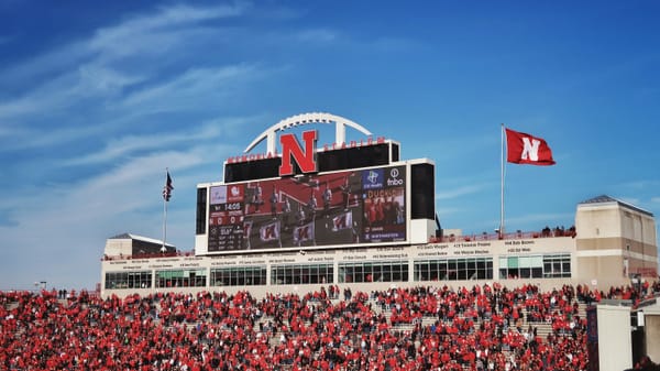 A clear view of a stadium scoreboard surrounded by fans during daylight. 